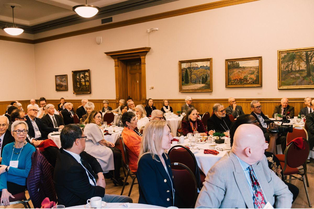 Guests sit at round tables, facing forward to listen to the speaker.