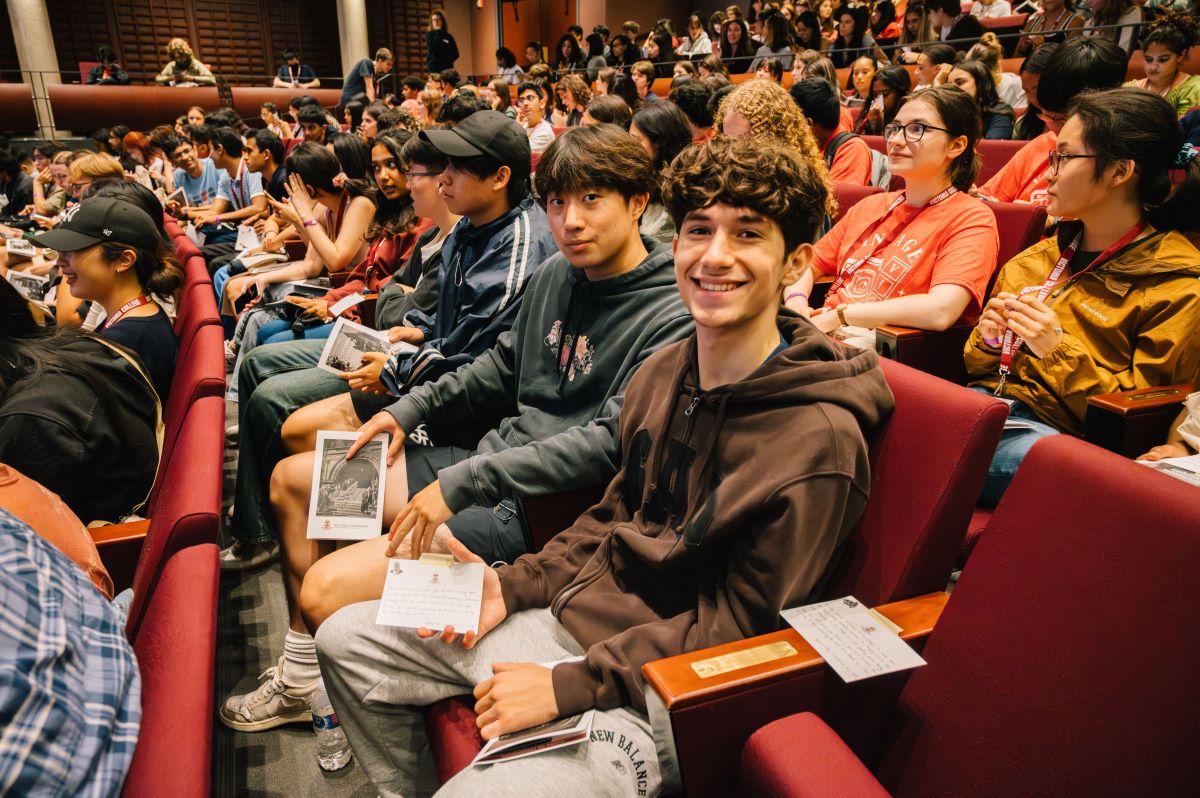 Two smiling first-year students look at the camera, holding handwritten messages from alumni in their hands.