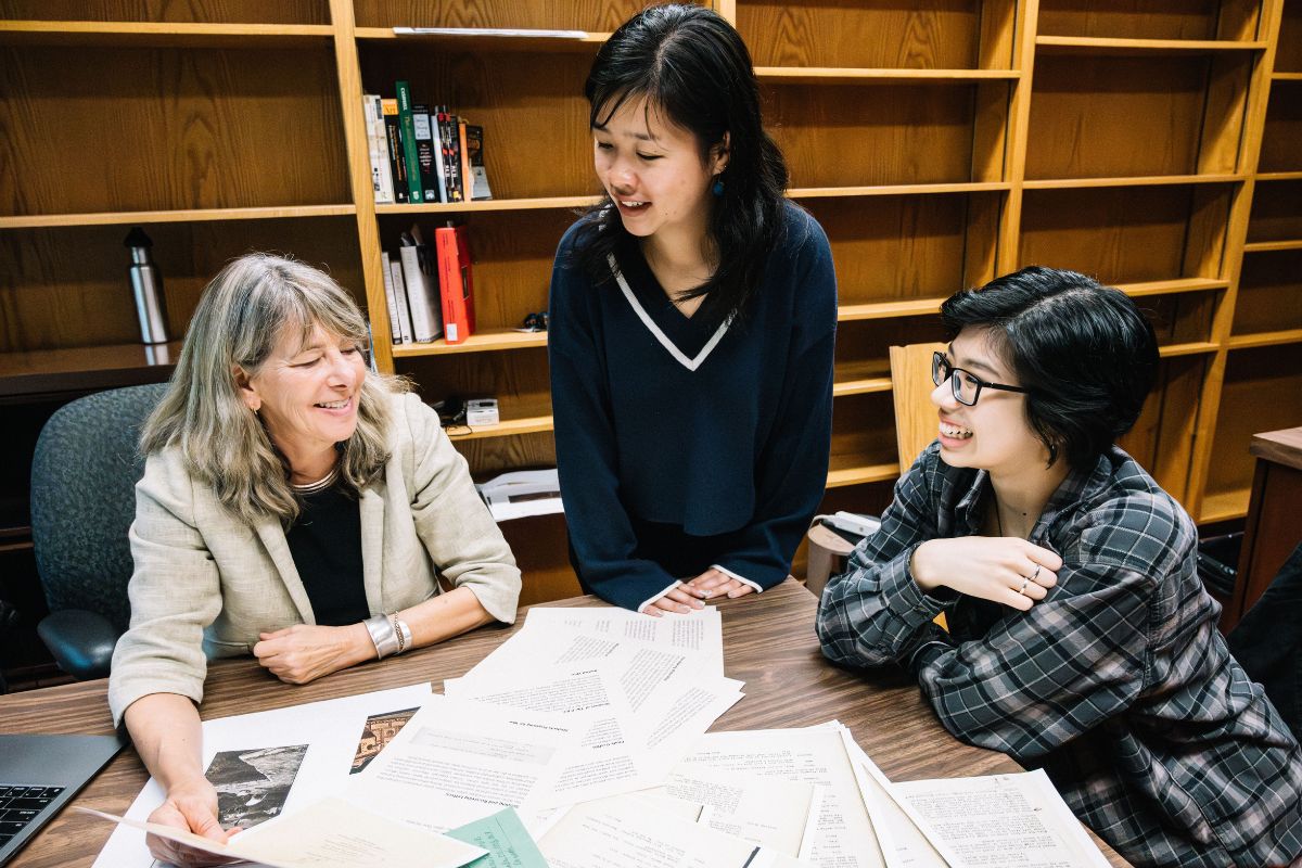 Professor Sutton and two of her student curators, Emily Fan and Eunice Der, sit at a table and discuss items to feature in their display.