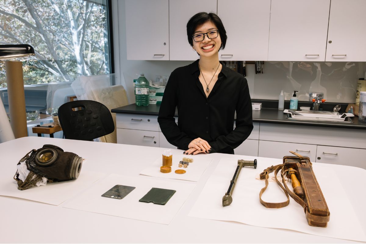 Student Eunice Der stands in front of an assortment of First World War artifacts, which are laid out on a white table.